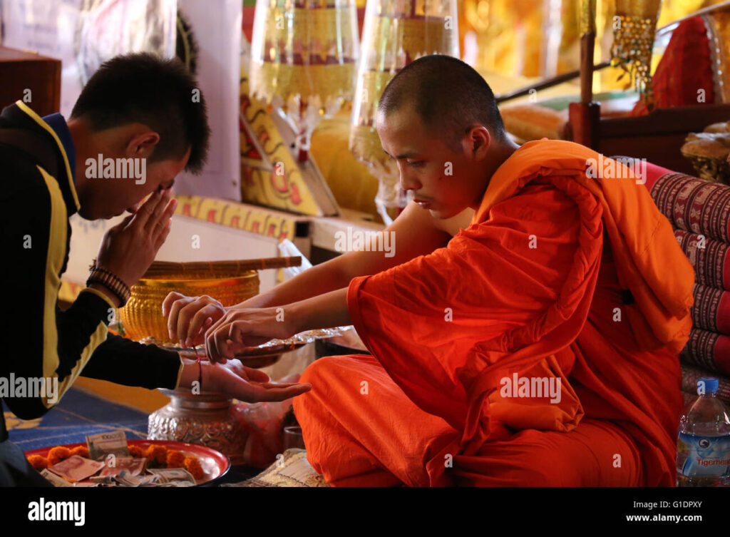 A man receiving the sai sin from a monk who then offers a prayer